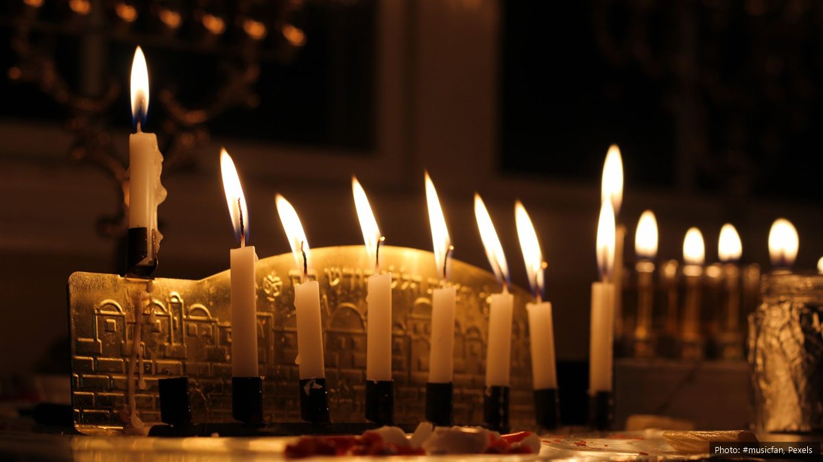 Hanukkah 2026 in South Africa: Dates, Candle Times and Is It a Public Holiday? A brass Hanukkah menorah with eight white candles and the helper candle lit in a dark room