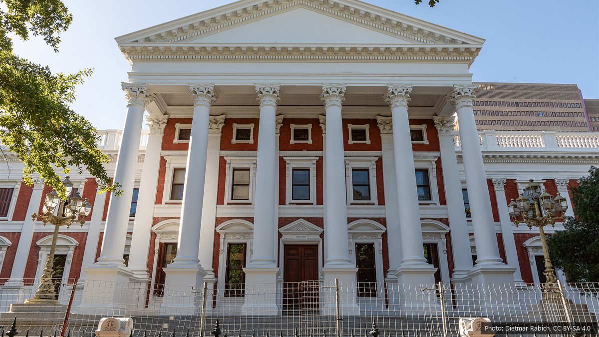 The white-columned front of the Parliament of South Africa building in Cape Town behind a black iron fence