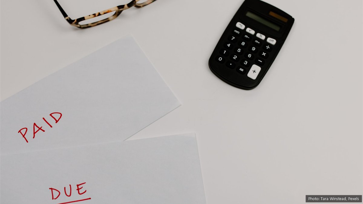Two white sheets of paper with PAID and DUE written in red, next to a black calculator and a pair of glasses