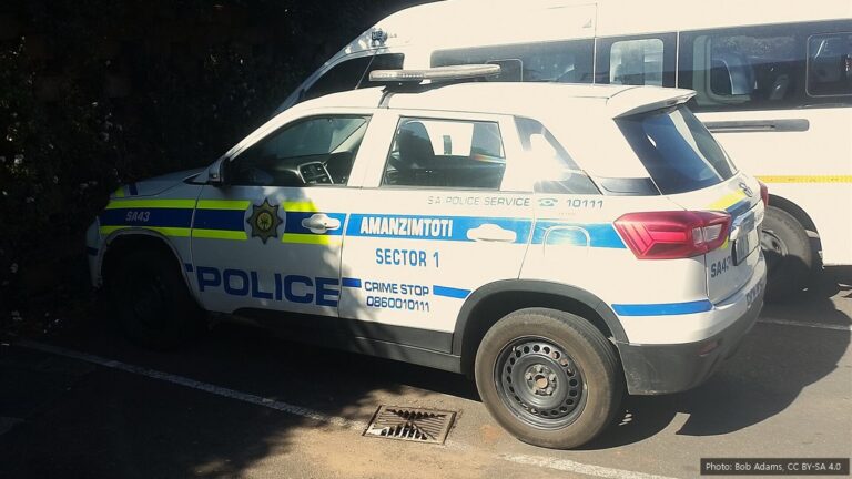SAPS Recruitment 2026/27: 5,500 Police Trainee Posts, Requirements and How to Apply A white South African Police Service patrol vehicle with blue and yellow markings of the Amanzimtoti station, parked next to a white minibus