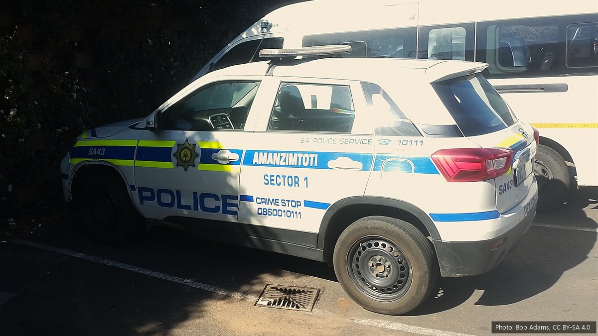 A white South African Police Service patrol vehicle with blue and yellow markings of the Amanzimtoti station, parked next to a white minibus